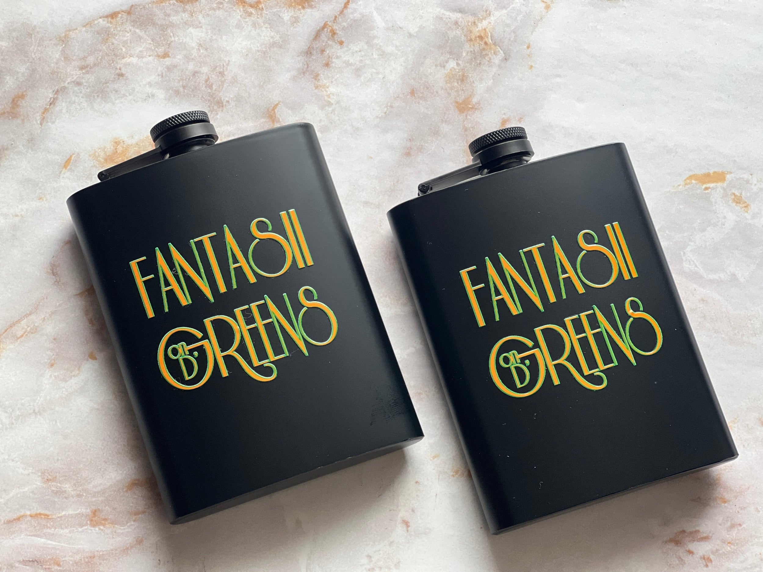 Two matte black company branded hip flasks with screw-top lids, printed with the company name 